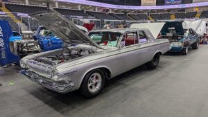 Classic silver muscle car with its hood open at a car show.