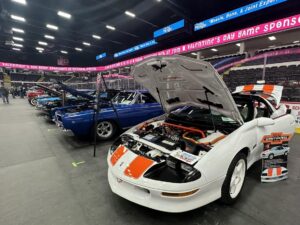 Classic cars showcased at an indoor auto event with open hoods.