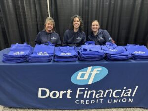 Three women at a Dort Financial Credit Union booth with blue bags.