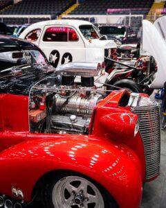Vintage red car with exposed engine at a classic car show.