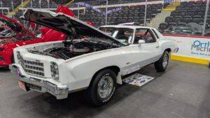 Classic white muscle car with open hood at a car show.