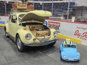 A vintage yellow VW Beetle with its hood open at a car show.