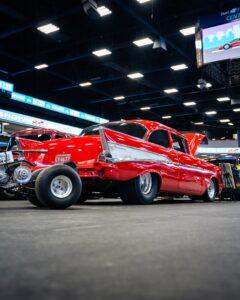 A classic red drag racing car at an indoor car show.