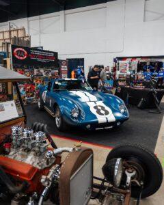 Classic blue race car with white stripes displayed at an indoor car show.