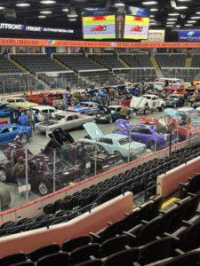 Indoor car show with numerous classic and custom vehicles on display.