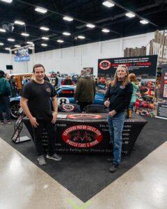 Two women at a booth promoting a wrestling-related product at a convention.