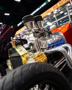 Close-up of a shiny, detailed engine on a custom car under bright lights.