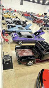 Classic muscle cars displayed indoors with custom grills and open hoods.