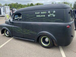 A vintage black van with green flames and 'Rat Rod Relics' painted on the window.