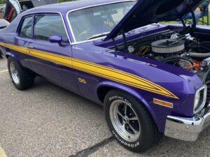 Classic purple muscle car with yellow racing stripes and open hood.