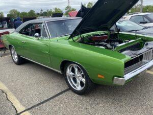 Classic green muscle car with open hood at a car show.