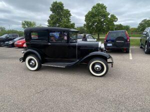 A vintage black car parked in a lot with trees in the background.