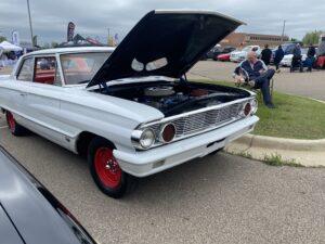 Classic white vintage car with red wheels and open hood at a car show.