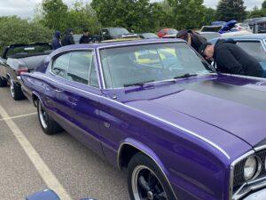 A classic purple muscle car parked in a lot with other vehicles.