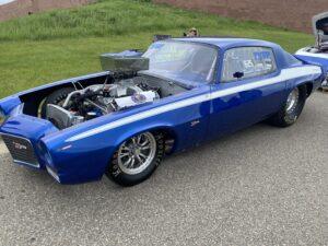 A blue vintage race car with its hood open, showing the engine.