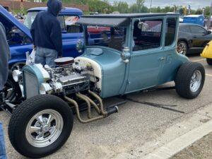 A vintage hot rod with exposed engine and custom exhaust pipes.