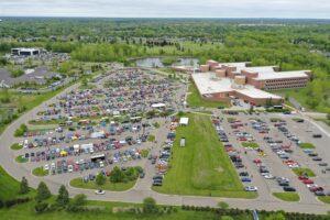 A large shopping mall parking lot filled with cars and surrounded by greenery.