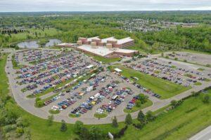 A large shopping mall with a packed parking lot surrounded by greenery.