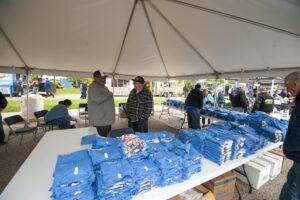 Volunteers organize blue t-shirts under a tent at an outdoor event.