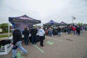 People queue outside tents at a community event on a cloudy day.