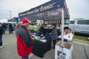 People engaging at a booth for American Classic Car Events under a canopy tent.