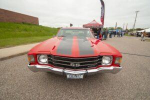 Classic red muscle car with black racing stripes at a car show.