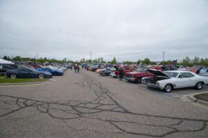 Wide parking lot with classic cars and people on a cloudy day.