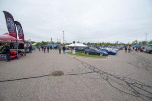 People gather at an outdoor car show on a cloudy day.