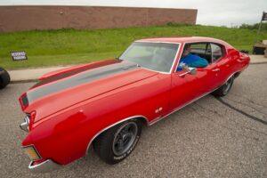 Classic red muscle car parked outdoors with black racing stripes.