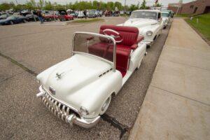 A unique white limousine styled like a classic car with red interior seating.