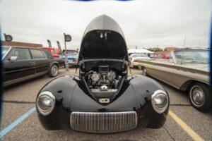 Classic black car with hood open, showcasing the engine at a car show.