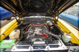 Close-up of a classic car engine under the hood with yellow exterior.