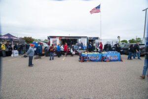 People gather at a community event with booths and an American flag.