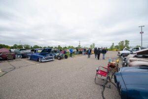 People gather outdoors around classic cars on a cloudy day.