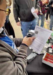 Person reading a printed document with a coffee cup in hand at a busy table.
