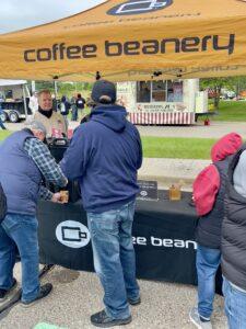 People gathered at a Coffee Beanery outdoor booth at a park.