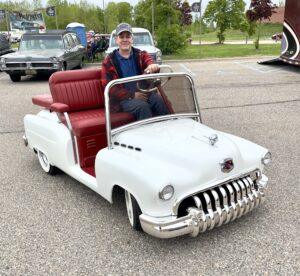 Man driving a vintage-style miniature white car with a big smile.