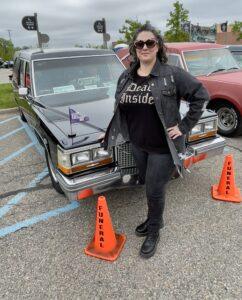 Woman in black outfit posing by a decorated car with orange cones.