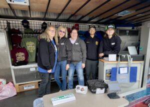 Five people standing behind a table with various items displayed.