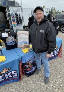 A man stands beside a promotional table with banners and merchandise.