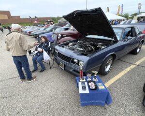 A classic car with its hood open at a car show, surrounded by people.