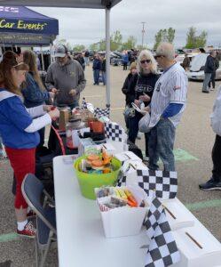 People gather at a booth with colorful baskets and checkered flags outdoors.