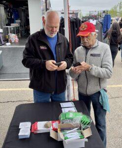 Two elderly men exchanging information at an outdoor event booth.