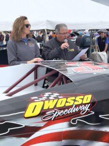 Two people speaking by a race car at Owosso Speedway event.