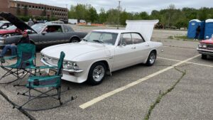 Classic white muscle car with hood open at a parking lot.