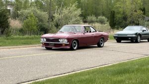 A classic maroon muscle car driving on a suburban road.