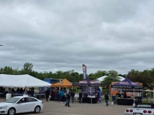 Crowd at an outdoor event with tents and cloudy skies.