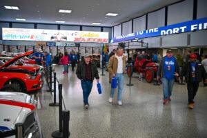 Shoppers walking in a busy indoor market or store with bright lighting.
