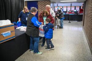 Adults and children interacting at an indoor event with informational booths.