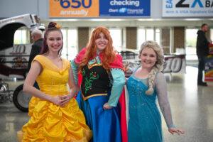 Three women dressed as Disney princesses posing and smiling.